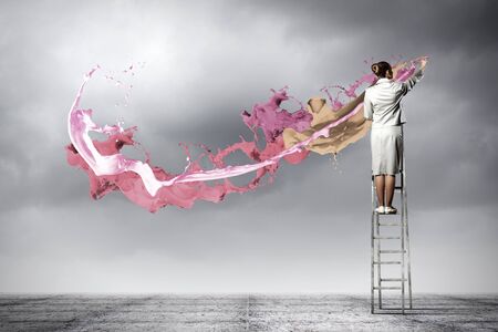 Young woman standing on ladder drawing splashes with fingerの写真素材