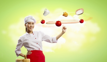 Asian female cook making pizza standing against color backgroundの写真素材