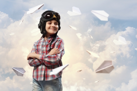 Image of little boy in pilots helmet with paper airplanes in backgroundの写真素材