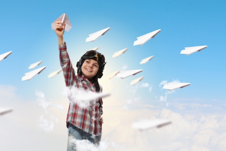 Image of little boy in pilots helmet playing with paper airplaneの写真素材