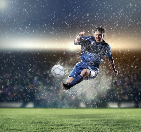 football player in blue shirt striking the ball aloft at the stadium under the rainの写真素材