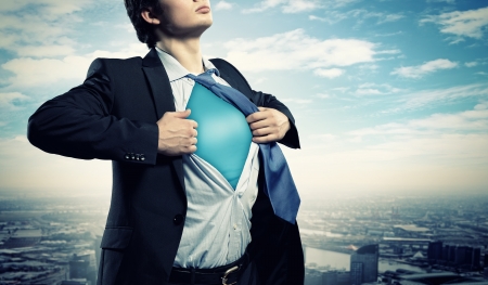 Image of young businessman showing superhero suit underneath his shirt standing against city backgroundの写真素材