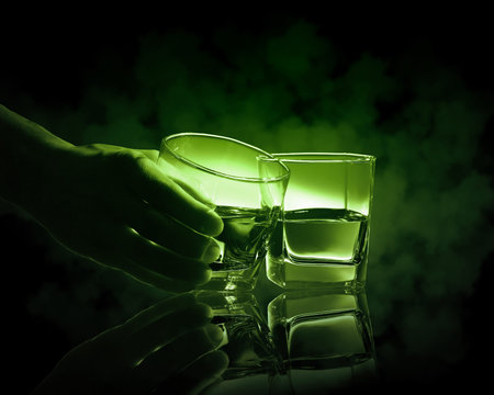 Hand holding one of two glasses of green absinth