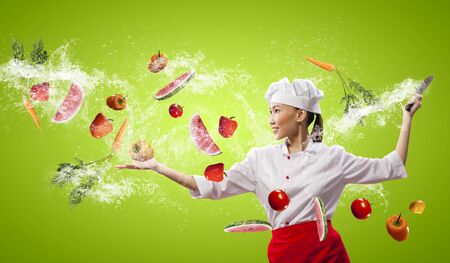 Asian female cook with knife cutting fruits and vegetables in airの写真素材
