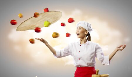 Asian female cook making pizza standing against color backgroundの写真素材
