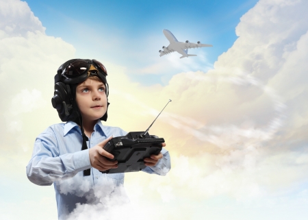 Image of little boy in pilots helmet playing with toy radiocontrolled airplane against clouds backgroundの写真素材
