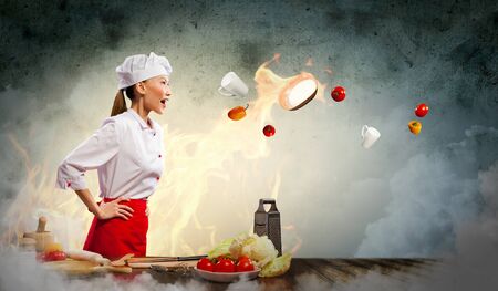 Asian female cook in anger with flyung vegetables against color background with shine effectsの写真素材