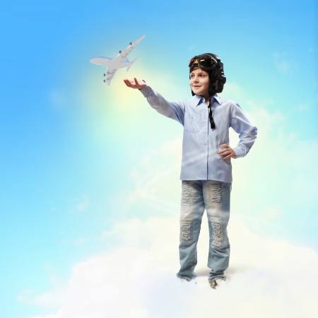 Image of little boy in pilots helmet playing with toy airplane against clouds backgroundの写真素材