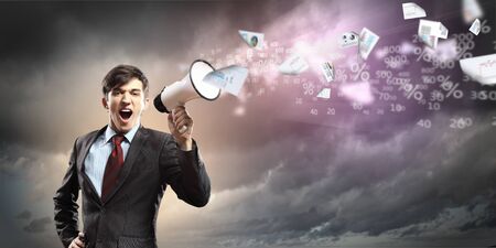 young businessman in black suit screaming into megaphoneの写真素材