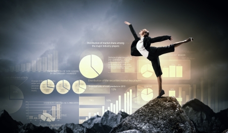 young businesswoman standing on one leg atop of mountain against diagram backgroundの写真素材