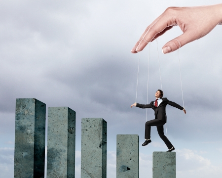 Businessman marionette on ropes controlled by puppeteer walking on barsの写真素材