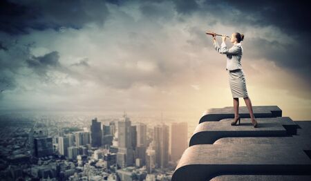 Image of businesswoman looking in telescope standing a top of buildingの写真素材