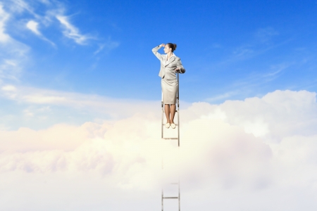 Businesswoman standing on ladder looking into distance against cloudy backgroundの写真素材