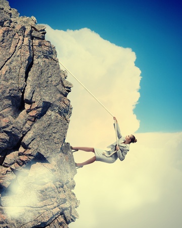 businesswoman climbing steep mountain hanging on ropeの写真素材