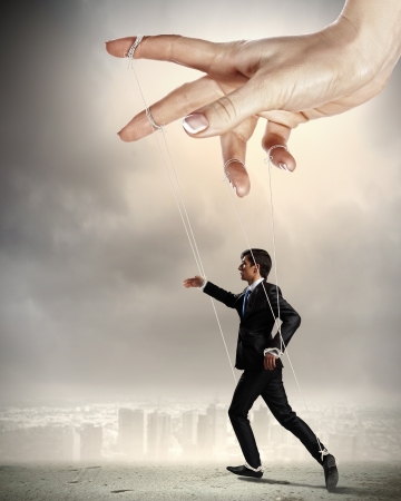 Businessman marionette on ropes controlled by puppeteer against city backgroundの写真素材
