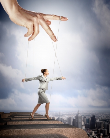 Businesswoman marionette on ropes controlled by puppeteer against city backgroundの写真素材