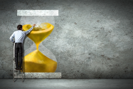 Businessman on ladder pointing at sandglass picture on wallの写真素材