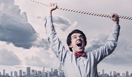 Image of businessman hanging on rope against city backgroundの写真素材