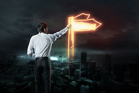 Businessman draws a light road sign on the dark skyの写真素材