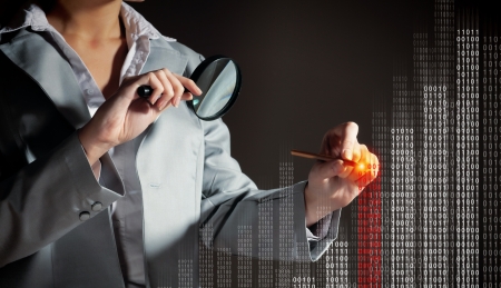 Businesswoman with magnifier glass examining binary codeの写真素材