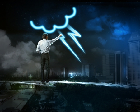 Businessman draws a glowing signs in the dark skyの写真素材