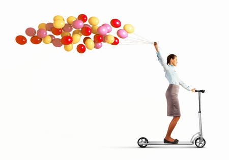 Image of young woman riding scooter with bunch of balloons in handの写真素材