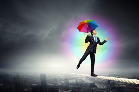 Businessman in black suit with umbrella balancing on ropeの写真素材