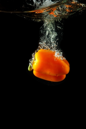 Colored orange paprika in water splashes on black backgroundの写真素材