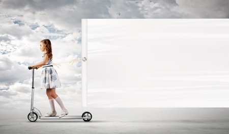 Little girl riding scooter and pulling blank bannerの写真素材