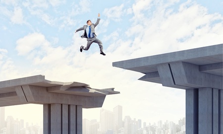 Businessman jumping over a gap in the bridge as a symbol of bridgeの写真素材