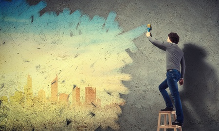 Young man painting a yellow colour cityscape on the wallの写真素材