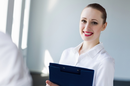 Image of young businesswoman holding folder and talking to colleagueの写真素材