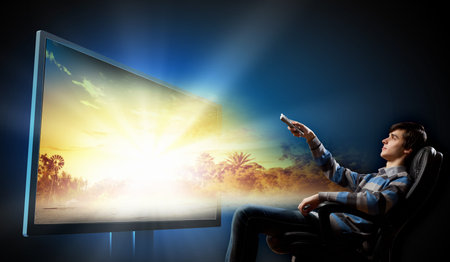 Young man in armchair with click watching TV