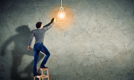 Young man with an electric light bulb against the wallの写真素材