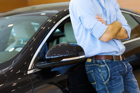 Handsome young man consultant at car salon standing near car