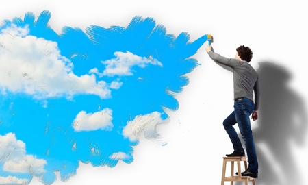 Young man drawing a cloudy blue sky on the wallの写真素材