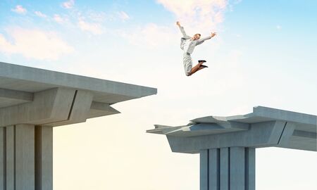 Young woman jumping over a gap in the bridge as a symbol of riskの写真素材