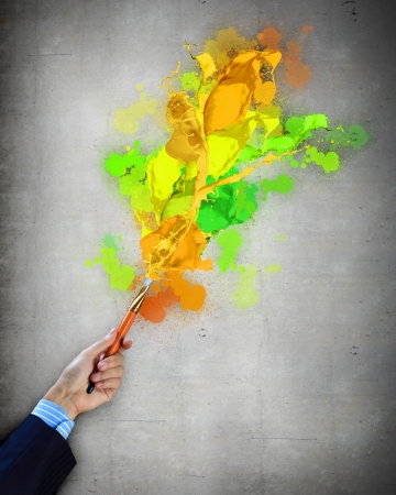 Close-up of human hand holding paint brush making colorful paint splashesの写真素材