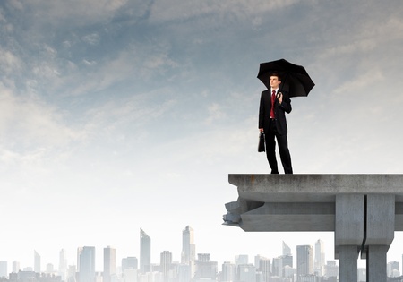 Young businessman with umbrella standing on bridgeの写真素材
