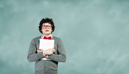 Young man in glasses standing and holding papers against blackboardの写真素材