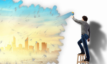 Young man painting a yellow colour cityscape on the wallの写真素材