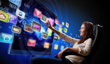 Young woman in armchair pushing icon on media screenの写真素材