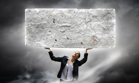 Image of young businesswoman holding burden above headの写真素材
