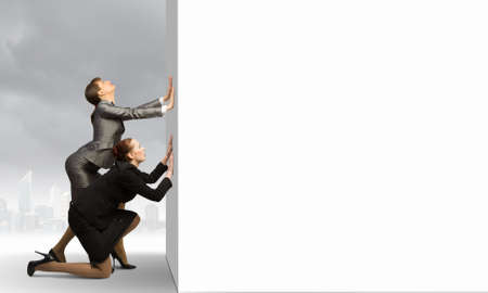 Image of two businesswomen pushing blank wall  Place for textの写真素材