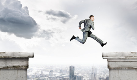 Image of young businessman jumping over gap in bridgeの写真素材