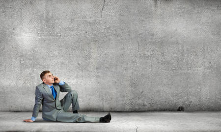 Image of young businessman with mobile phone sitting on floorの写真素材