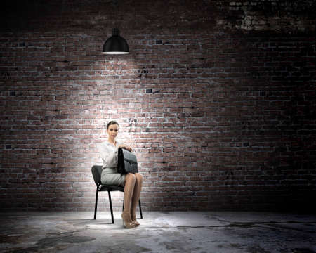 Image of young businesswoman sitting on chair under spot of lightの写真素材