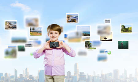 Image of cute boy holding photo camera standing among photosの写真素材