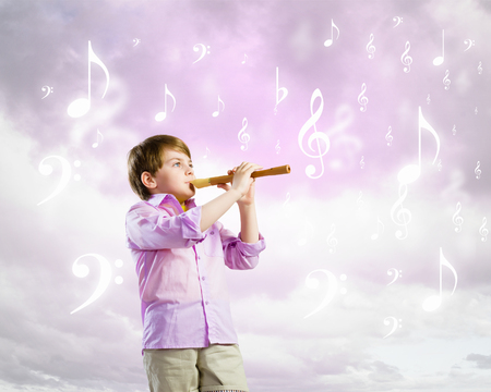 Image of little cute boy playing on flute against cloudy backgroundの写真素材