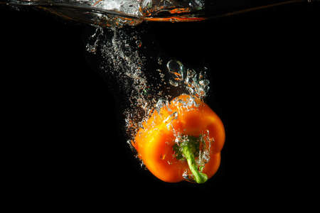 Colored orange paprika in water splashes on black backgroundの写真素材